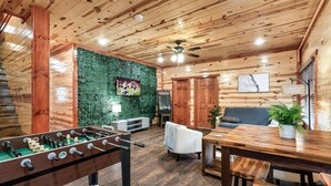 Une pièce avec un plancher en bois, une table de baby-foot, un canapé, une table à manger et un téléviseur.