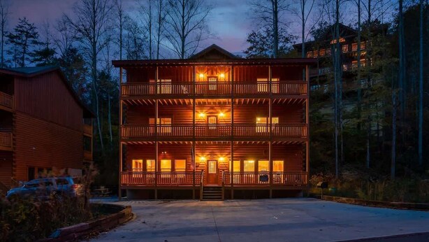 Un chalet en bois à plusieurs étages, doté d’un balcon au deuxième étage et entouré d’arbres.
