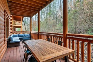 A wooden deck with a table and chairs, a sofa, and a balcony overlooking a forested area. - 6-Bedroom All-Ensuite Cabin with Indoor Pool & Theater Near Dollywood (Pigeon Forge)