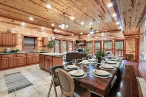 A wooden cabin interior with a dining area, kitchen, and large windows.