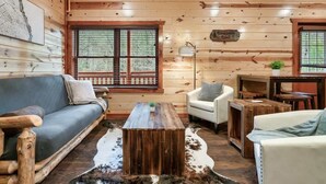 L’intérieur d’une cabane en rondins, avec un canapé, un fauteuil, une table basse et un tapis en peau de vache.