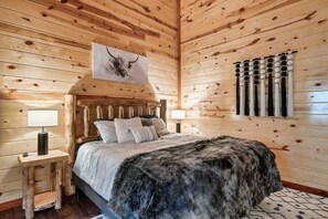 A wooden-paneled room with a bed, a wall-mounted artwork, and a window with vertical blinds.