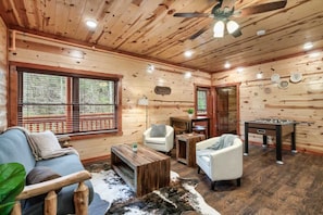 A cozy cabin interior with a sofa, armchairs, a coffee table, a foosball table, and a large window. - 6-Bedroom All-Ensuite Cabin with Indoor Pool & Theater Near Dollywood (Pigeon Forge)