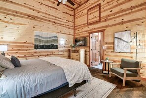 A wooden cabin bedroom with a bed, a chair, a small table, and artwork on the walls. - 6-Bedroom All-Ensuite Cabin with Indoor Pool & Theater Near Dollywood (Pigeon Forge)