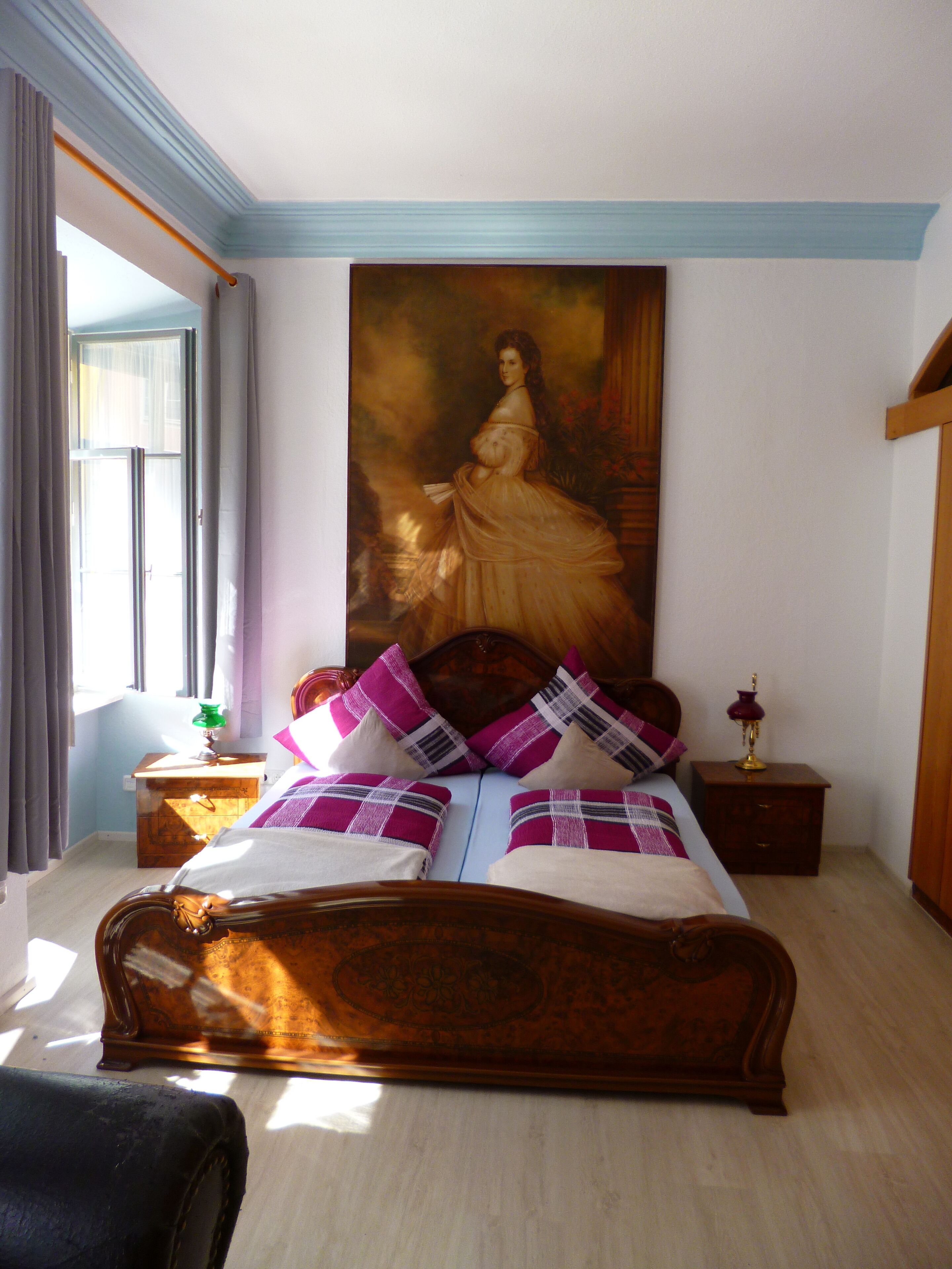 A bedroom with a large bed, a nightstand, a lamp, and a painting on the wall.