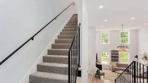 Eine moderne Treppe mit schwarzer Handläufung führt zu einem Wohnbereich mit Sofa, Couchtisch und einer Deckenleuchte.