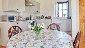 A kitchen with white cabinets, a microwave, a toaster, and a sink. There is a vase with flowers on the dining table. - 2 bedroom accommodation in Glencraigs, near Campbeltown (Glencraigs, near Campbeltown)