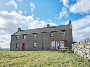 A two-story stone house with a red door, a glass door entrance, and a stone wall to the right. - 2 bedroom accommodation in Glencraigs, near Campbeltown (Glencraigs, near Campbeltown)