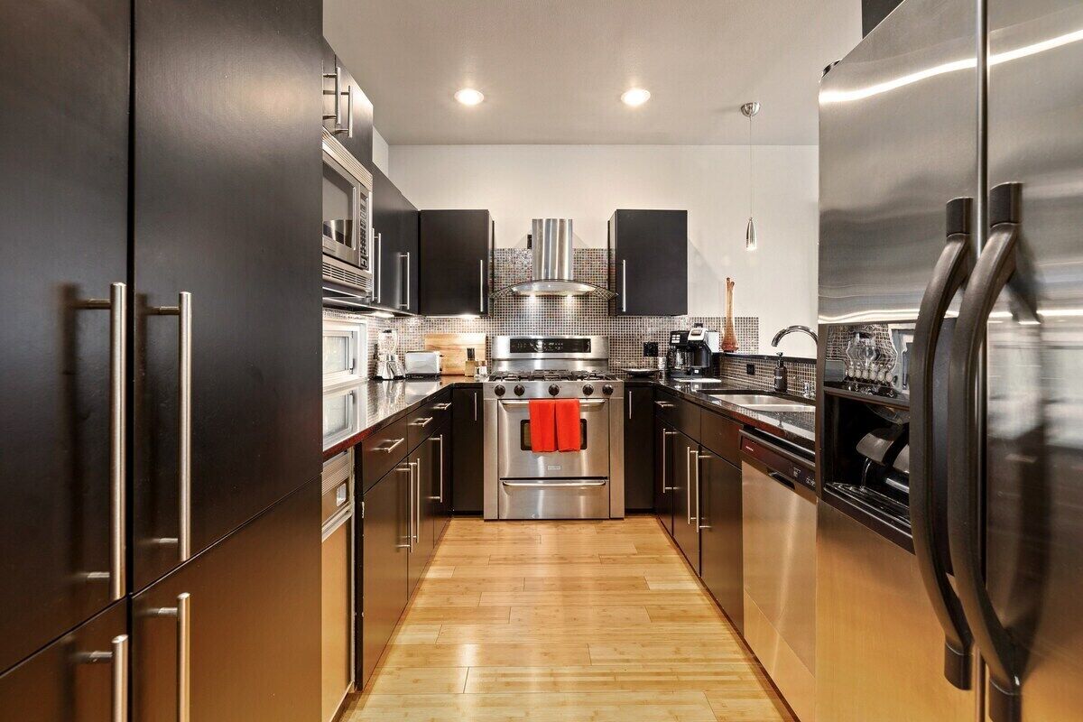 Una cocina moderna con electrodomésticos de acero inoxidable, piso de madera y muebles oscuros.