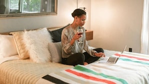 A person sitting on a bed with a laptop, holding a glass. - The Abshier - Near U of A - Quiet Getaway (Fayetteville)