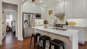 A modern kitchen with white cabinetry, stainless steel appliances, and a central island with stools. - The SoFay Farmhouse - 1 mi From U of A (Fayetteville)