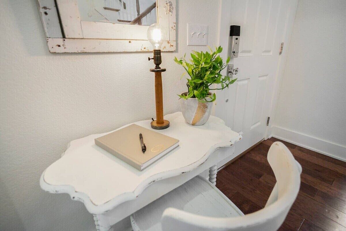 Et hvidt, udsmykket skrivebord med en lampe, en notesbog og en pen. En potteplante står på væggen ved siden af skrivebordet.