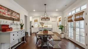 A spacious kitchen with a wooden dining table, white cabinetry, and large windows. - The SoFay Farmhouse - 1 mi From U of A (Fayetteville)