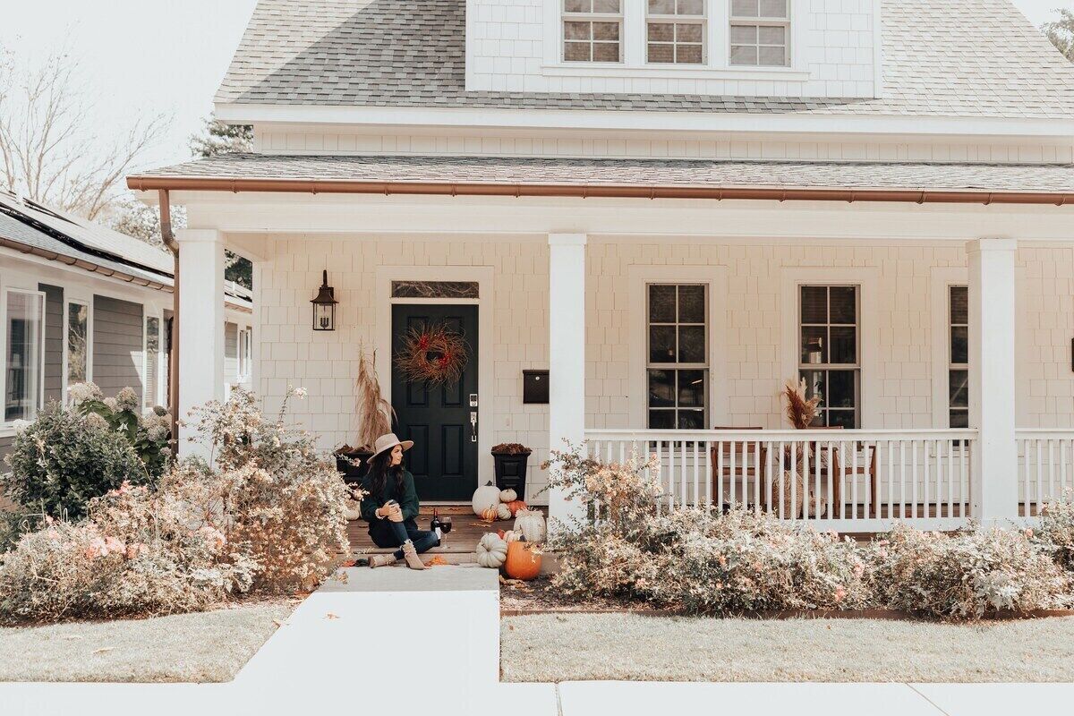 A white two-story house with a front porch, a black door, and a wreath on the door.