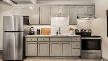 A modern kitchen with grey cabinets, a stainless steel refrigerator, a built-in oven, and a tiled backsplash.