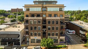 A multi-story building with a modern architectural design, featuring a mix of glass and brick facades, and a parking lot in front. - The East View - Downtown - Steps to Dickson (Fayetteville)