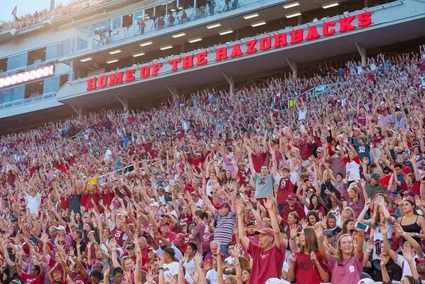 A stadium filled with spectators, with a sign reading "Home of the Razorbacks".