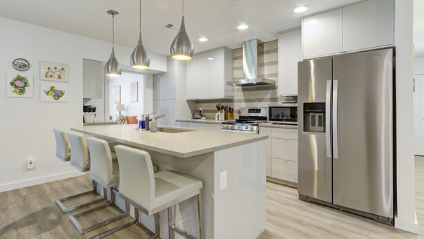 A modern kitchen with a central island, stainless steel appliances, pendant lighting, and a view into the dining area. - Crown - A Birdy Vacation Rental (San Antonio)