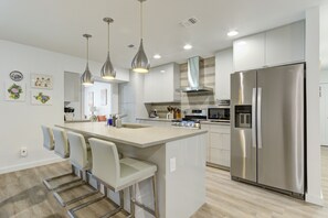 A modern kitchen with a central island, stainless steel appliances, pendant lighting, and a view into the dining area.