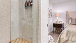 A modern bathroom with a glass-enclosed shower, a wooden shelf, and a patterned floor. - Crown - A Birdy Vacation Rental (San Antonio)