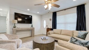 A modern living room with a round coffee table, beige sofas, a flat-screen TV, and a ceiling fan. - Crown - A Birdy Vacation Rental (San Antonio)