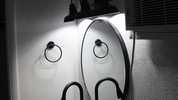 A bathroom with a wooden vanity, a mirror, and a wall-mounted air conditioning unit. - Holiday Lodge Motel (Sheridan)