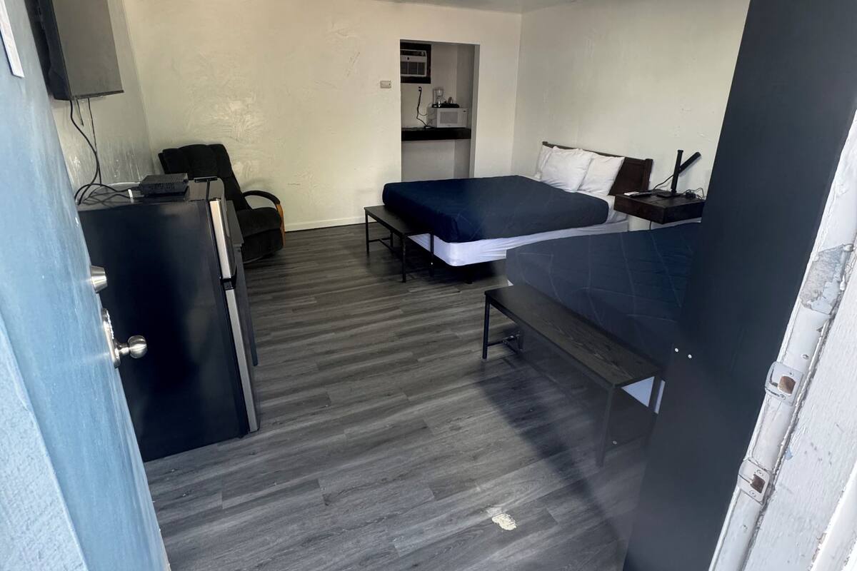 A compact room with a bed, a desk, a chair, and a small kitchenette.