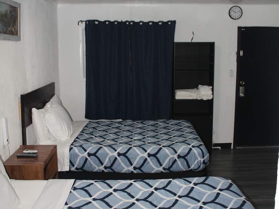 A room with two beds, a nightstand, a clock, and a door.