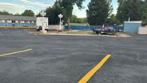 A parking lot with a yellow line marking, a blue building with a white door, and a small fenced area with a blue tarp. - Holiday Lodge Motel (Sheridan)