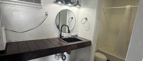 Un bagno piccolo con un mobile bagno in legno, uno specchio rotondo, un water e uno spazio doccia.