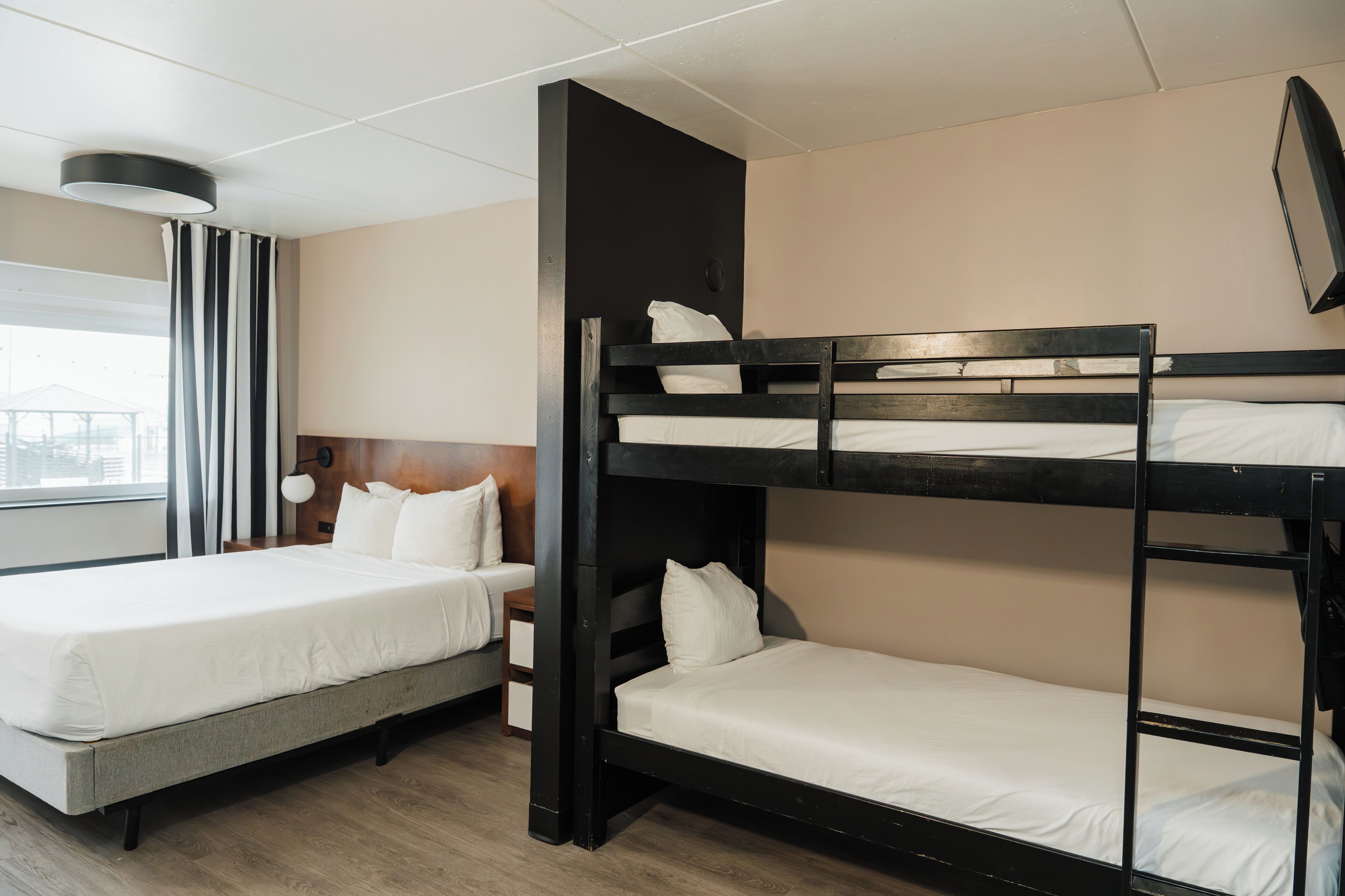 Habitación de hotel con literas, cama individual, mesita de noche y ventana con cortinas.