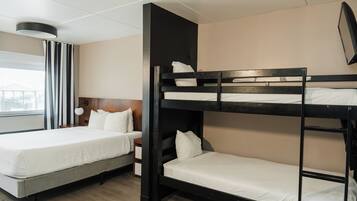 Habitación de hotel con literas, cama individual, mesita de noche y ventana con cortinas.