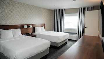 Una habitación de hotel con dos camas, cabecera de madera, un escritorio y un ventanal con cortinas.