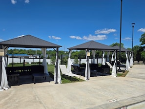 Two covered seating areas with benches, a paved walkway, and a clear blue sky.
