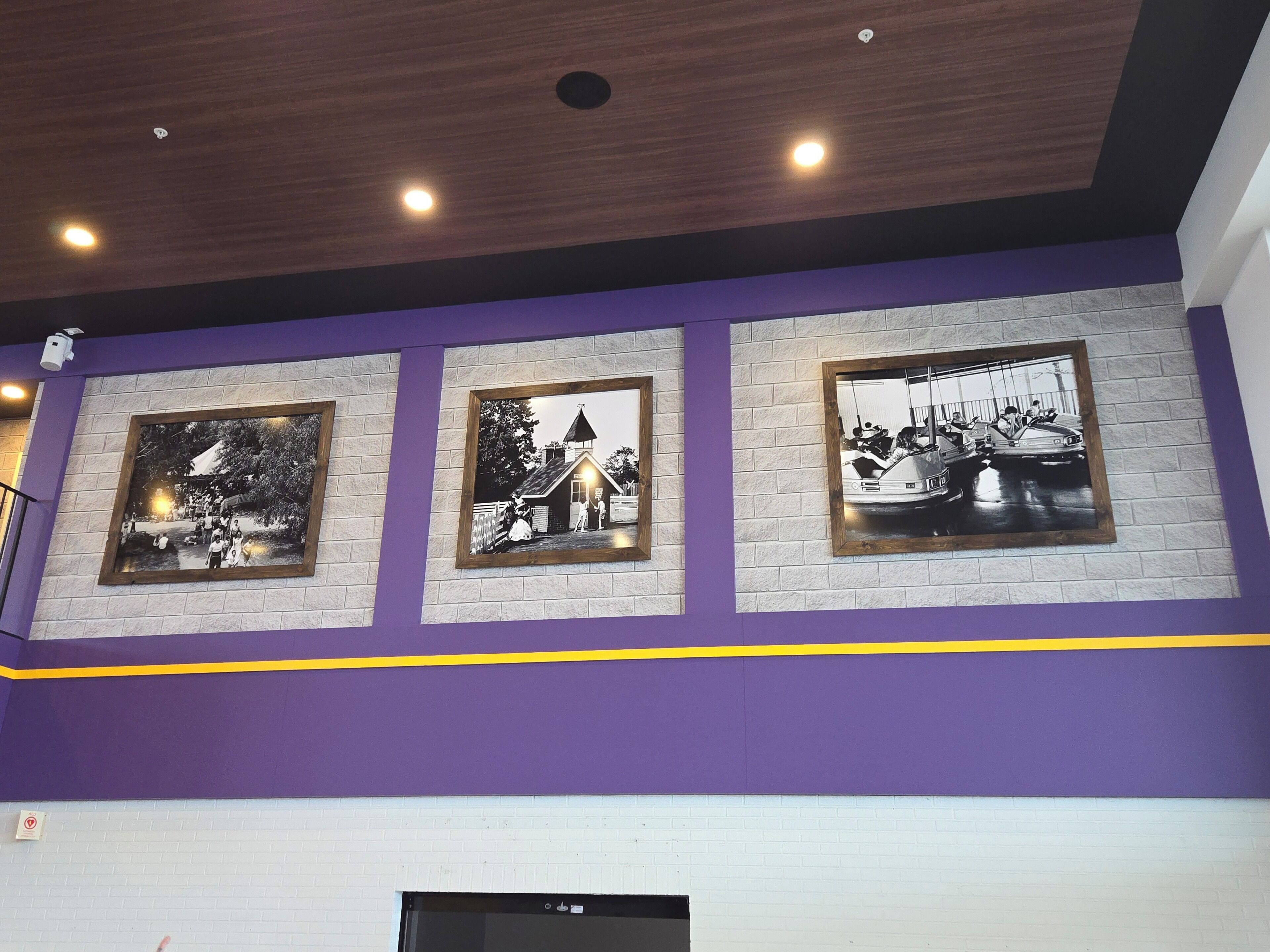 A wall with three framed black and white photographs, a purple accent wall, and a ceiling with recessed lighting.