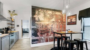 A modern kitchen with a large abstract mural, a dining area with stools, and a visible window with curtains.