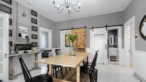 A dining area with a wooden table and black chairs, a chandelier, and a sign reading "POWDER ROOM" in the background.