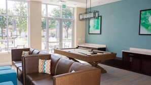 Una mesa de billar, un sofá y un armario en una habitación con ventanas grandes.