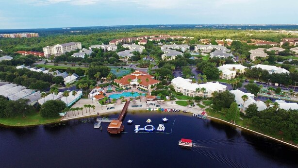 Vista aérea de un complejo turístico con piscina central, varias edificaciones y un puerto deportivo con barcos.