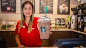 Una persona con uniforme rojo sosteniendo un café Starbucks con pajita verde.