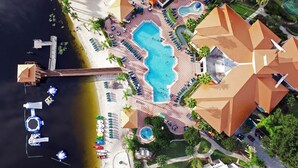Vista aérea de un resort con una piscina central, varias zonas de descanso y un muelle con barcos.