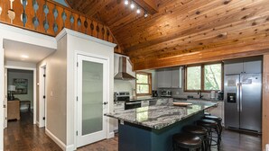 A modern kitchen with a large island, stainless steel appliances, and a wooden ceiling.