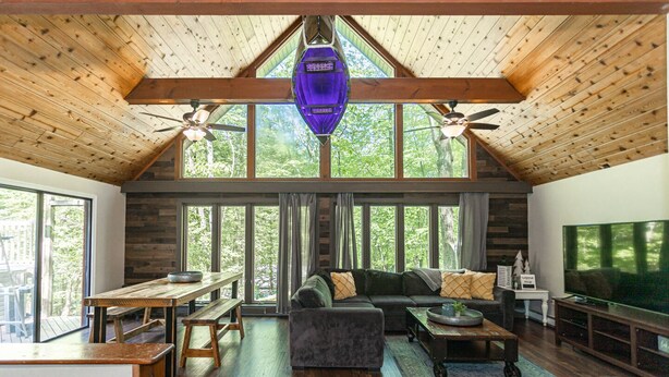 A spacious living area with a high ceiling, wooden beams, a large window, a sofa, a coffee table, and a television.