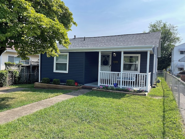 A single-story house with a front porch, a small garden, and a clear sky.