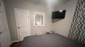 Une chambre à coucher avec un lit, un téléviseur fixé au mur, une porte et un miroir.