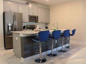 Cozinha moderna com ilha central, eletrodomésticos de aço inoxidável e banquetas azuis.