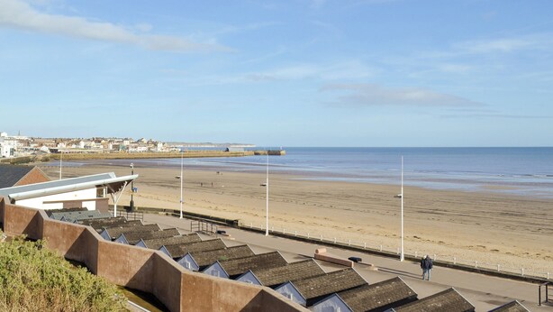Une vue sur la côte, avec une plage, une promenade et une rangée de maisons aux toits inclinés.