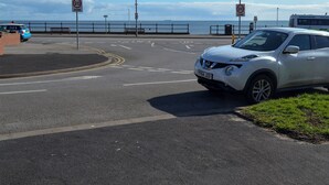 Une route côtière avec un panneau indiquant la limitation de vitesse, une voiture blanche et un autobus en arrière-plan.