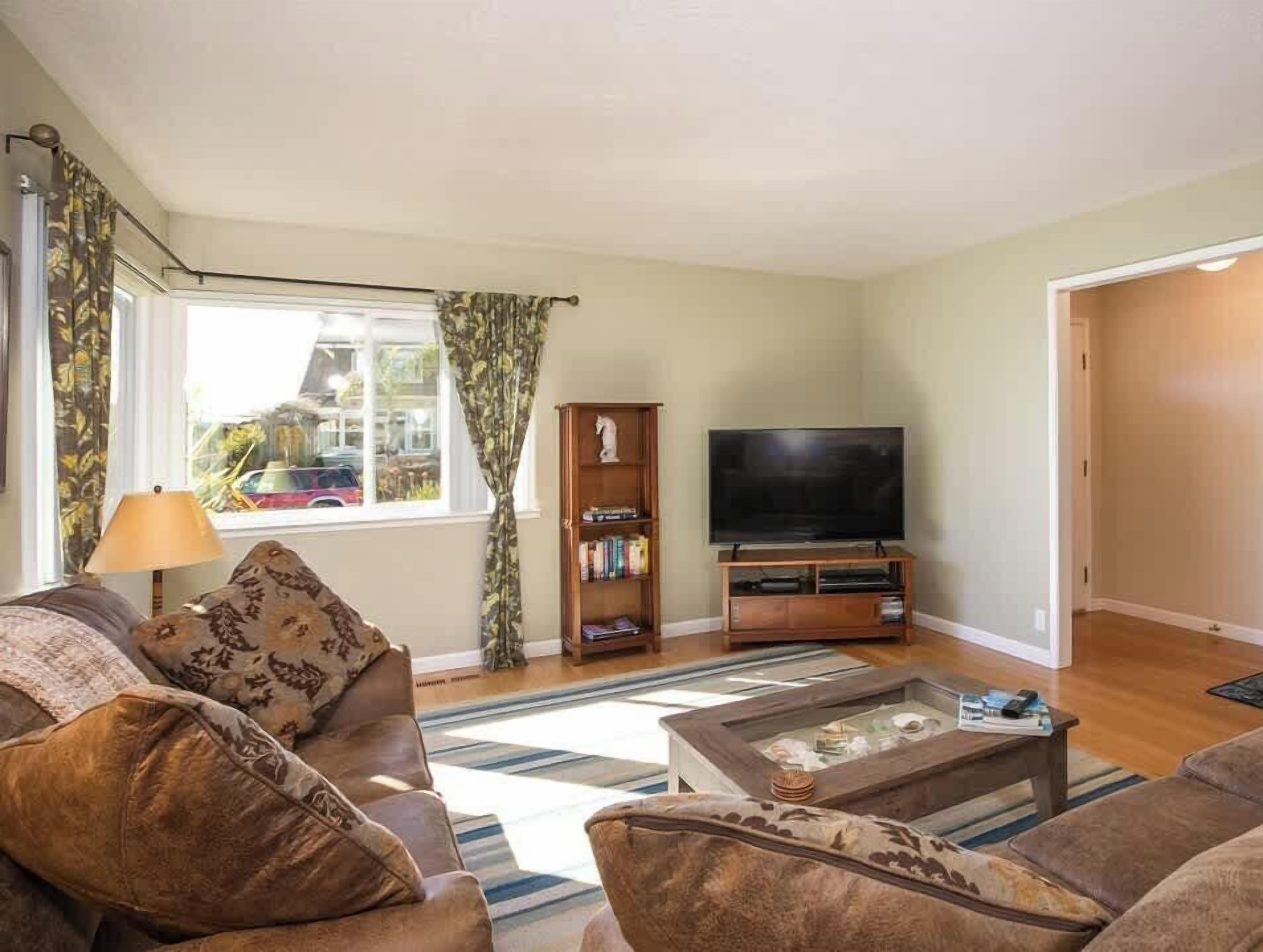 A living room with a sofa, a coffee table, a TV, a bookshelf, and a window with curtains.