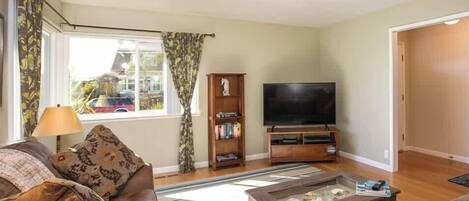 A living room with a sofa, a coffee table, a TV, a bookshelf, and a window with curtains.